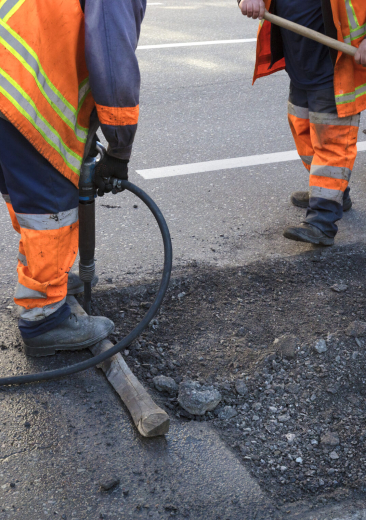 a brigade of servants for road maintenance removes the old asphalt with a jackhammer and shovels into the excavator cart in road construction